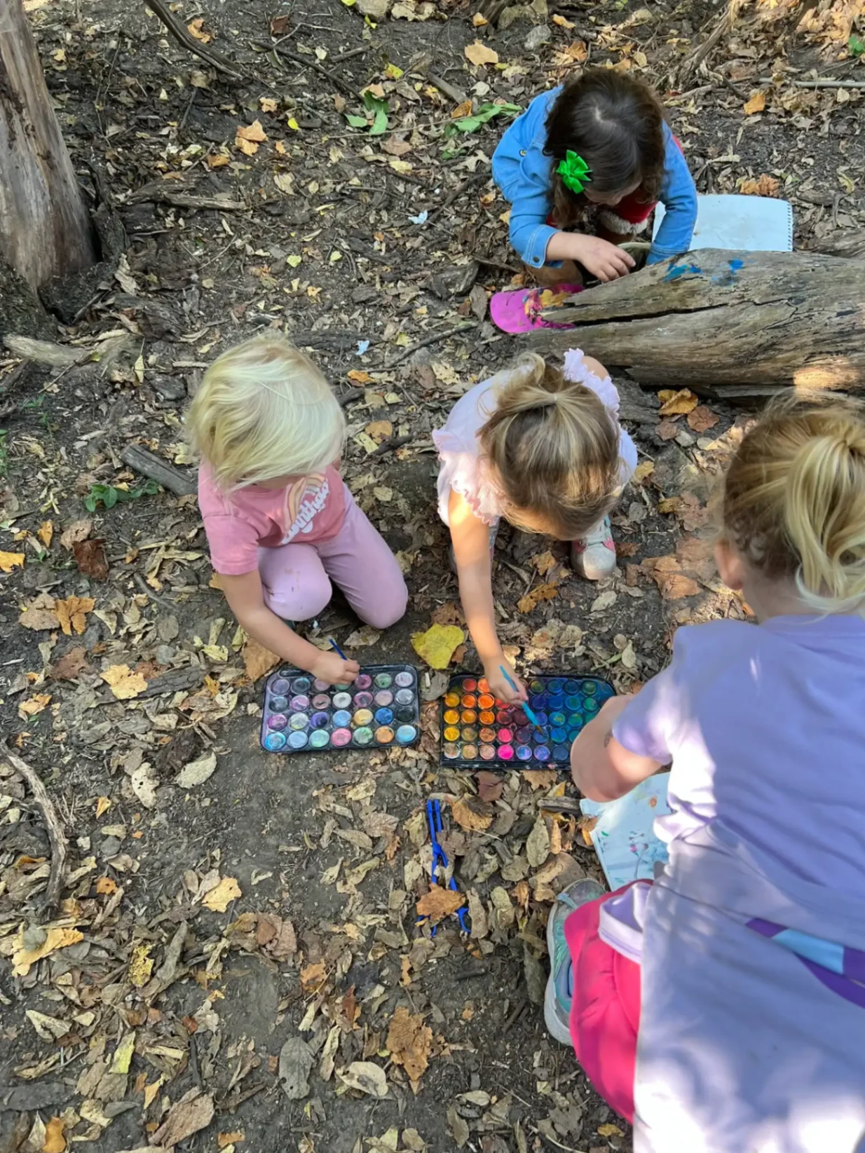 Children gathered around watercolor trays painting on the forest floor